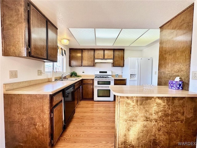 kitchen with light wood finished floors, a sink, a peninsula, white appliances, and under cabinet range hood