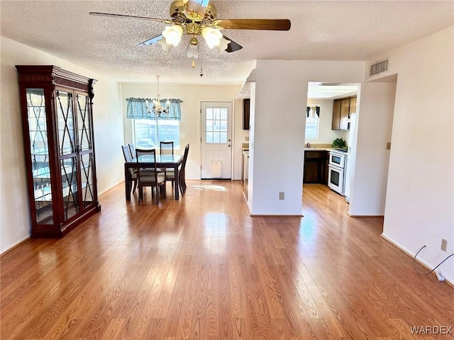 dining area featuring a textured ceiling, ceiling fan with notable chandelier, wood finished floors, visible vents, and baseboards