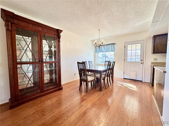 dining room featuring light wood-style floors, baseboards, a chandelier, and a textured ceiling