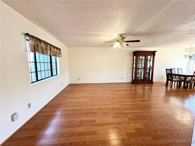 unfurnished living room featuring a textured ceiling, dark wood-type flooring, and ceiling fan with notable chandelier