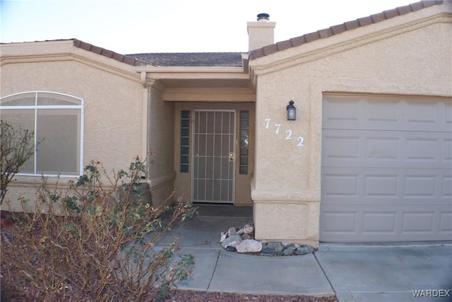 property entrance featuring a garage, a chimney, and stucco siding