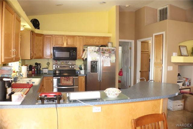 kitchen featuring a peninsula, dark countertops, appliances with stainless steel finishes, and a sink