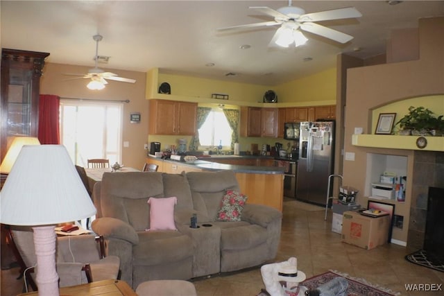 living area featuring a ceiling fan, lofted ceiling, a tiled fireplace, and light tile patterned floors