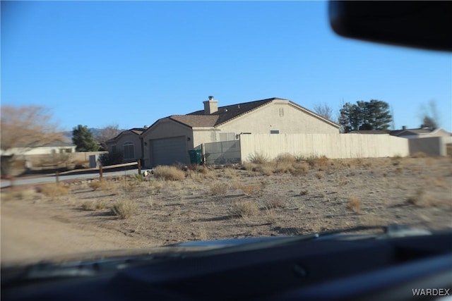 view of side of property with a garage, a chimney, fence, and stucco siding