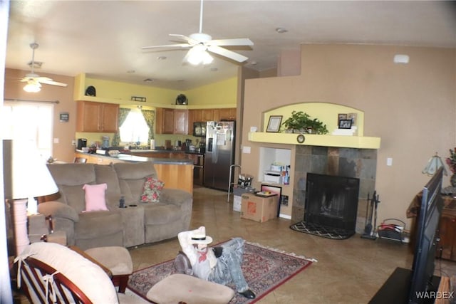 living area with a ceiling fan, vaulted ceiling, a tiled fireplace, and light tile patterned floors