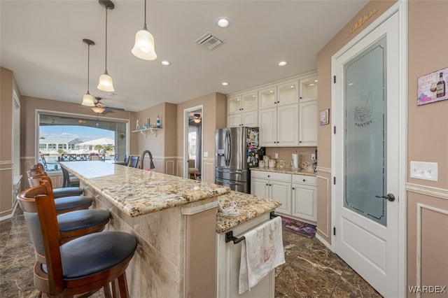 kitchen with visible vents, white cabinetry, a center island, stainless steel fridge, and glass insert cabinets