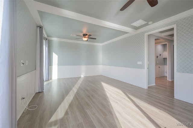 empty room with a ceiling fan, wainscoting, light wood-style flooring, and wallpapered walls