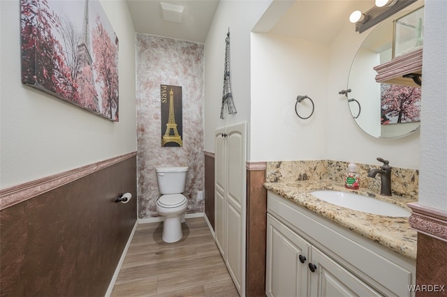 bathroom with a wainscoted wall, vanity, toilet, and wood finished floors