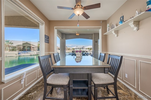 dining space featuring a wainscoted wall, ceiling fan, and a decorative wall