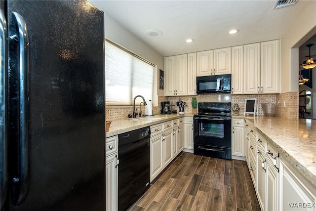 kitchen featuring black appliances, light stone counters, white cabinets, and a sink