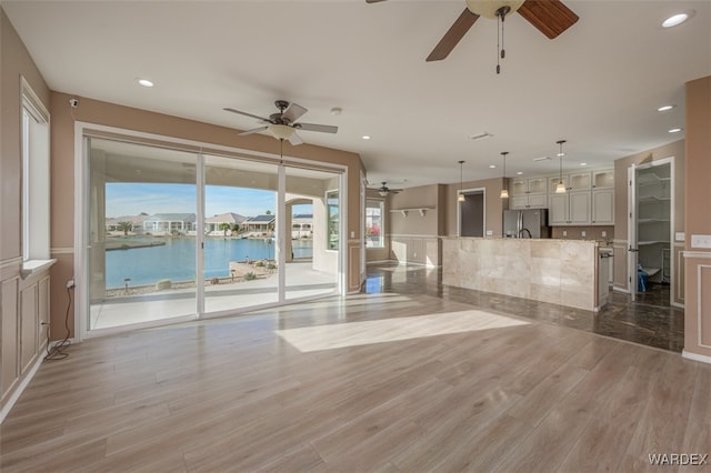 unfurnished living room featuring a water view, light wood-type flooring, ceiling fan, and recessed lighting