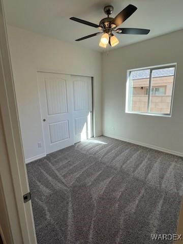 unfurnished bedroom featuring a ceiling fan, baseboards, dark colored carpet, and a closet