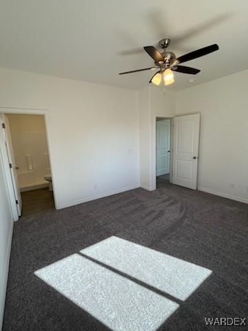 unfurnished bedroom featuring dark carpet, connected bathroom, a ceiling fan, and baseboards