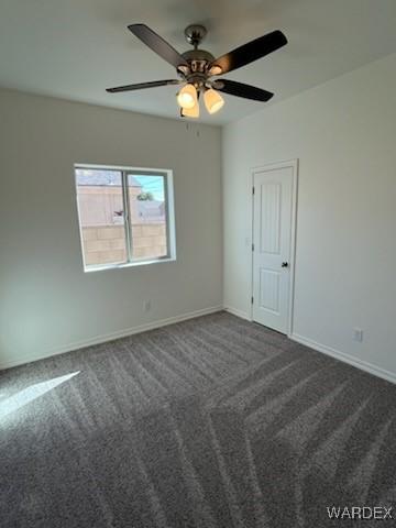 empty room featuring dark colored carpet, ceiling fan, and baseboards