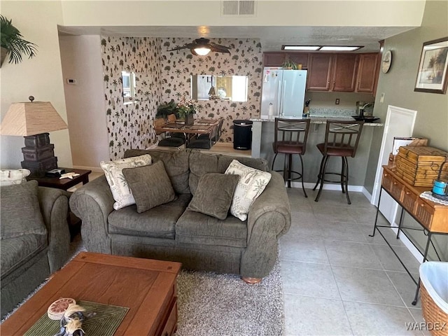 living area featuring light tile patterned floors, ceiling fan, visible vents, and baseboards