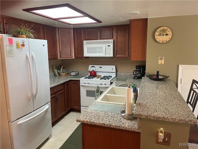 kitchen featuring a peninsula, white appliances, and a sink