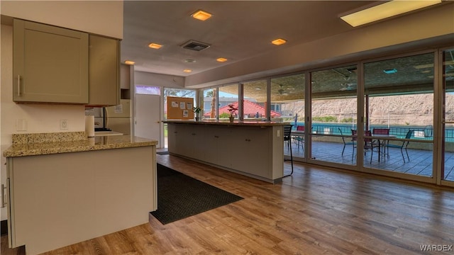 kitchen with light stone countertops, visible vents, wood finished floors, and gray cabinetry