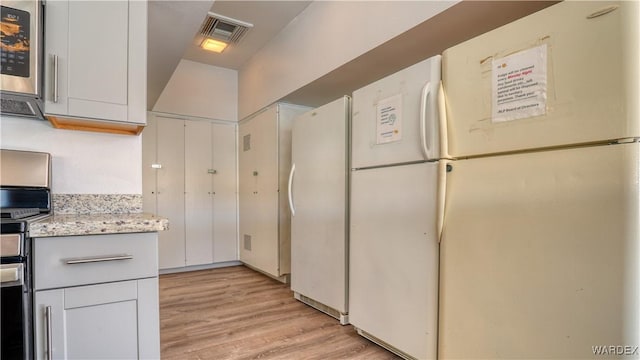 kitchen featuring light wood-style flooring, freestanding refrigerator, white cabinetry, and visible vents