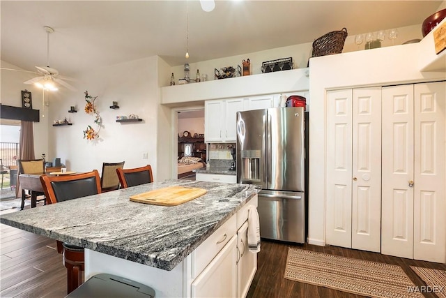 kitchen with stainless steel fridge, a breakfast bar, dark stone countertops, a center island, and white cabinetry