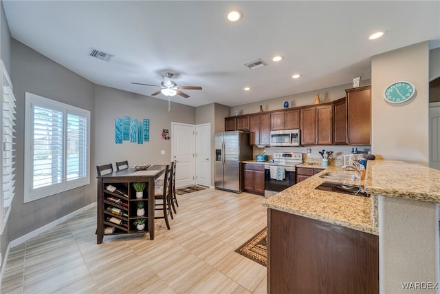 kitchen with appliances with stainless steel finishes, visible vents, a peninsula, and light stone countertops