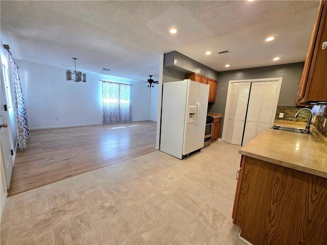 3166 E Thompson Ave, Kingman, AZ 86409 - kitchen featuring white fridge with ice dispenser, a sink, brown cabinets, open floor plan, and a textured ceiling
