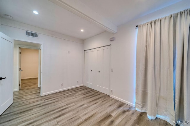 unfurnished bedroom with beam ceiling, light wood-style flooring, visible vents, and baseboards