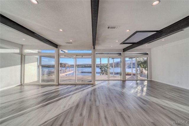 unfurnished living room with a water view, visible vents, light wood-type flooring, beamed ceiling, and baseboards