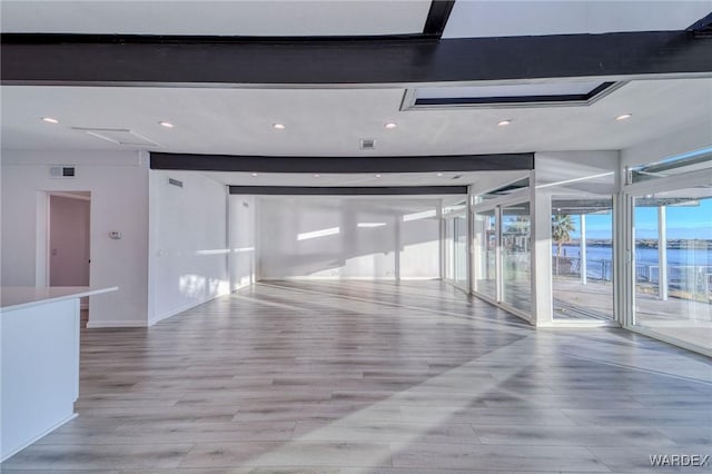 spare room with visible vents, light wood finished floors, a water view, and beam ceiling