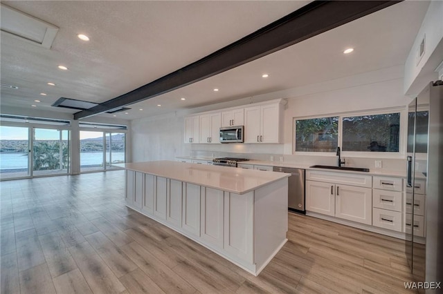 kitchen featuring a sink, white cabinets, open floor plan, light countertops, and appliances with stainless steel finishes