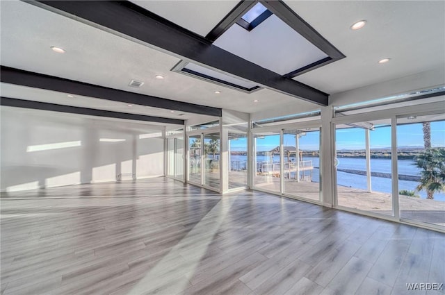 unfurnished room featuring recessed lighting, a water view, visible vents, light wood-style floors, and beamed ceiling