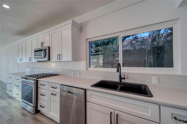 kitchen featuring white cabinetry, stainless steel appliances, a sink, and light countertops