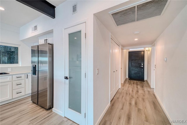 corridor featuring light wood finished floors, visible vents, and beam ceiling