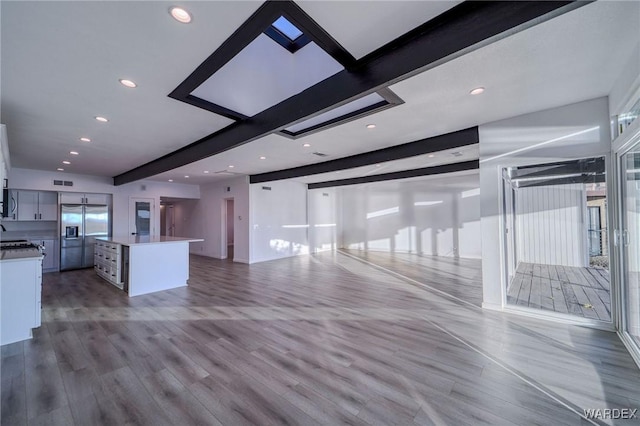 unfurnished living room featuring beam ceiling, recessed lighting, visible vents, a sink, and wood finished floors