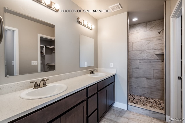 bathroom with a tile shower, double vanity, a sink, and visible vents