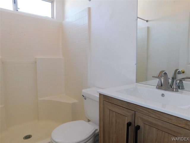 full bathroom with toilet, tiled shower, and vanity