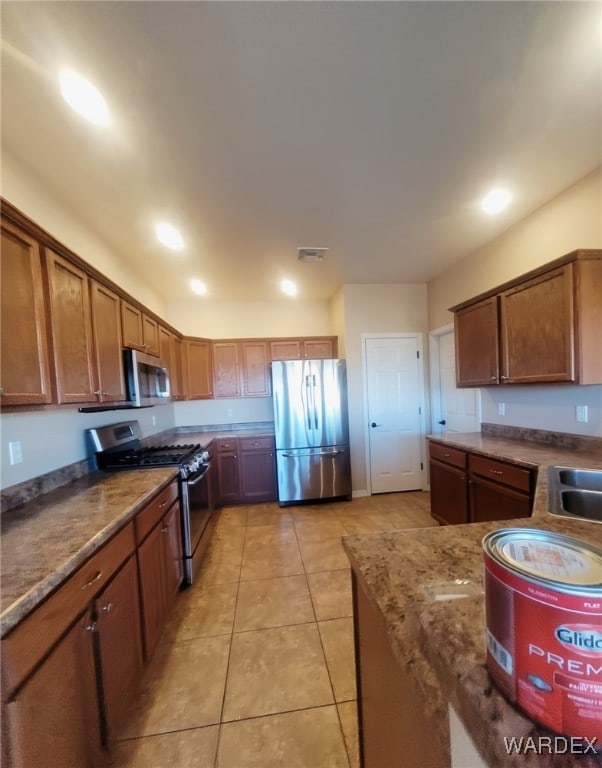 kitchen featuring light tile patterned floors, stainless steel appliances, visible vents, brown cabinets, and dark stone countertops