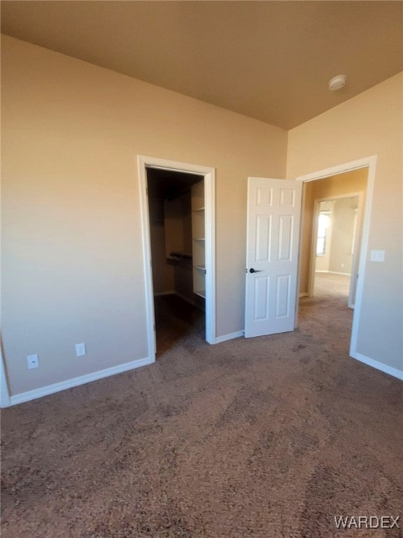 unfurnished bedroom featuring carpet floors, lofted ceiling, a spacious closet, and baseboards