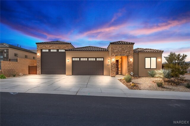 view of front of home with stucco siding, an attached garage, stone siding, driveway, and a tiled roof