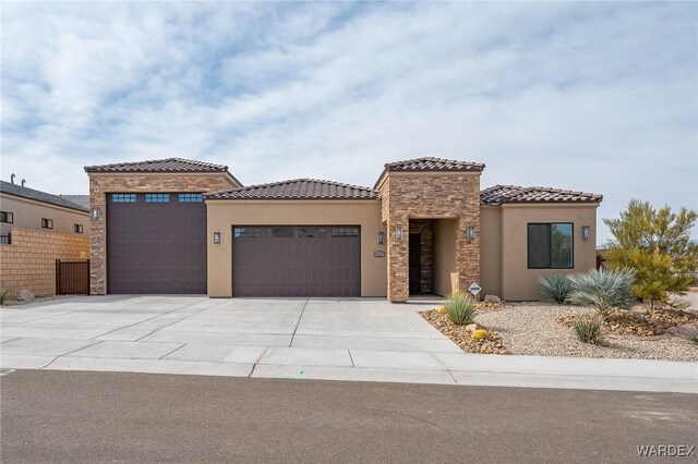 mediterranean / spanish house featuring a garage, concrete driveway, stone siding, a tiled roof, and stucco siding