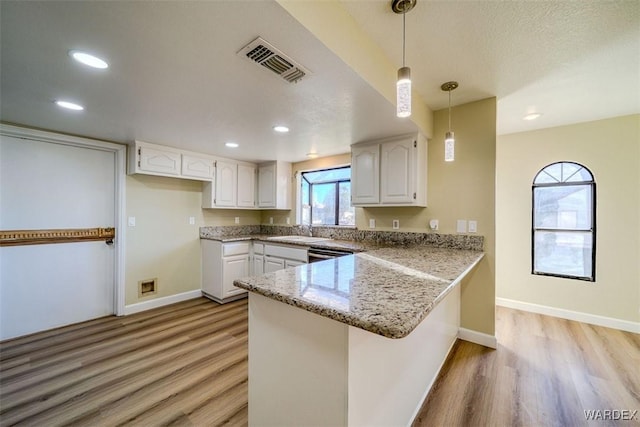 kitchen featuring stone countertops, visible vents, white cabinets, decorative light fixtures, and a peninsula