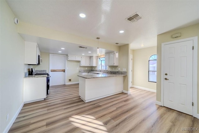 kitchen with visible vents, a peninsula, stainless steel appliances, a healthy amount of sunlight, and white cabinetry