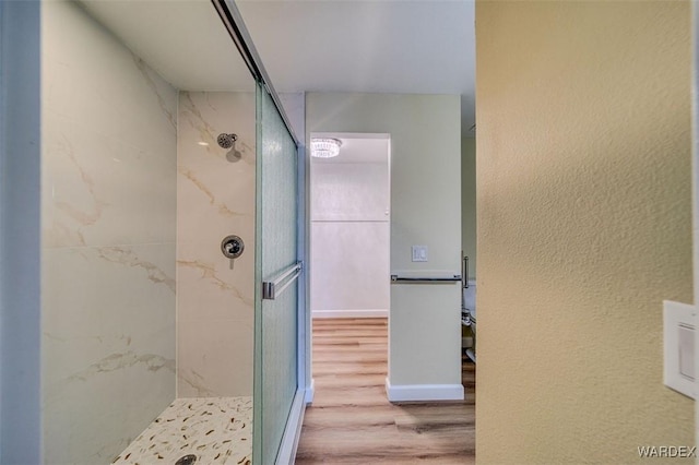 bathroom with a marble finish shower, wood finished floors, and a textured wall