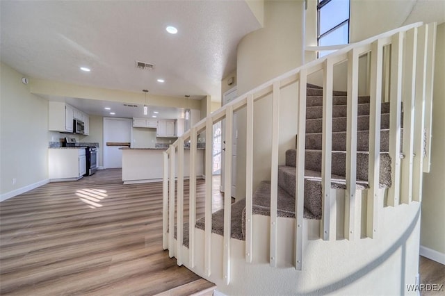 stairway with baseboards, wood finished floors, visible vents, and recessed lighting