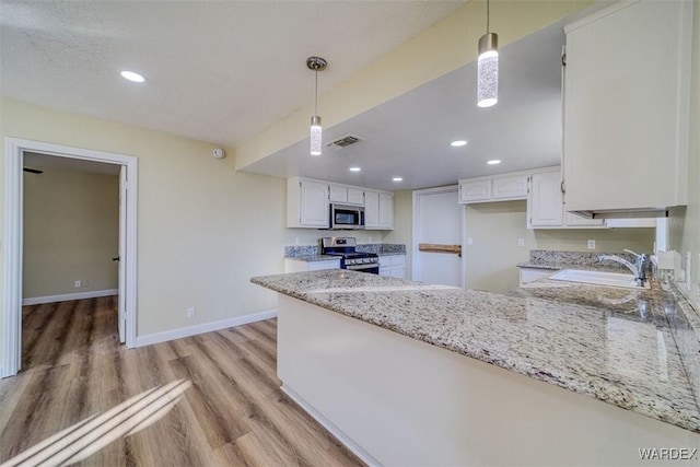 kitchen featuring hanging light fixtures, appliances with stainless steel finishes, white cabinetry, a sink, and light stone countertops