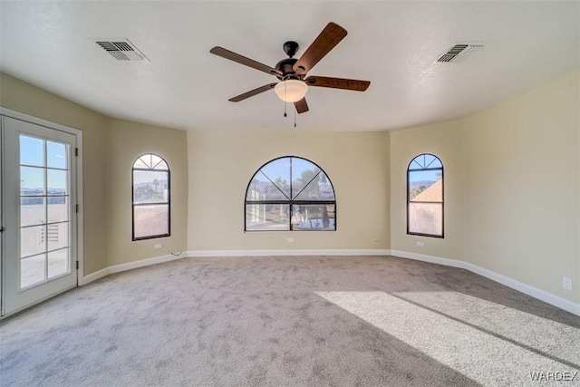 empty room with a ceiling fan, light colored carpet, visible vents, and baseboards