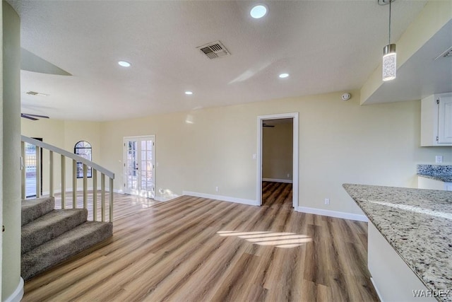 unfurnished living room featuring light wood-type flooring, visible vents, stairs, and baseboards