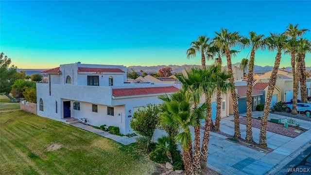 view of front facade featuring a garage, concrete driveway, a front yard, a mountain view, and stucco siding