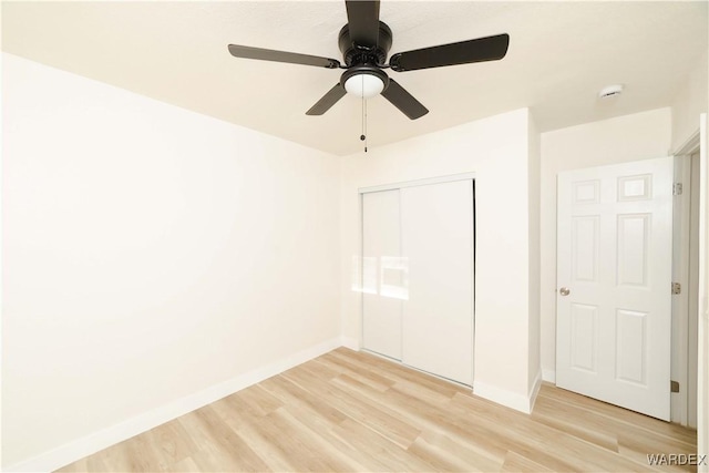 unfurnished bedroom featuring baseboards, ceiling fan, a closet, and light wood-style floors