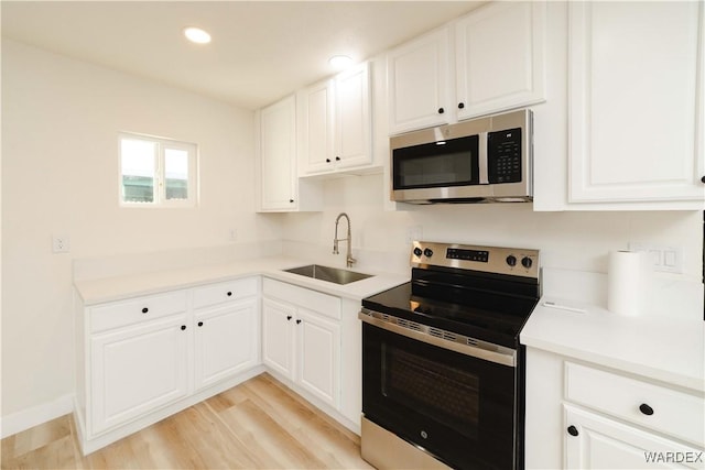 kitchen featuring appliances with stainless steel finishes, white cabinets, light countertops, and a sink