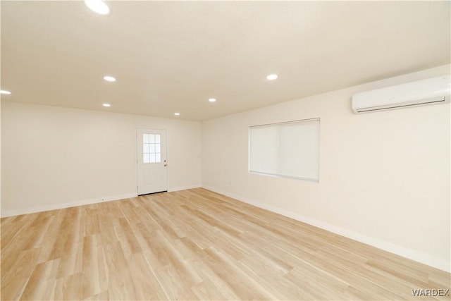 empty room featuring light wood-type flooring, recessed lighting, baseboards, and a wall mounted air conditioner